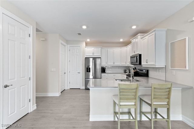 kitchen featuring a breakfast bar area, white cabinetry, appliances with stainless steel finishes, kitchen peninsula, and decorative backsplash