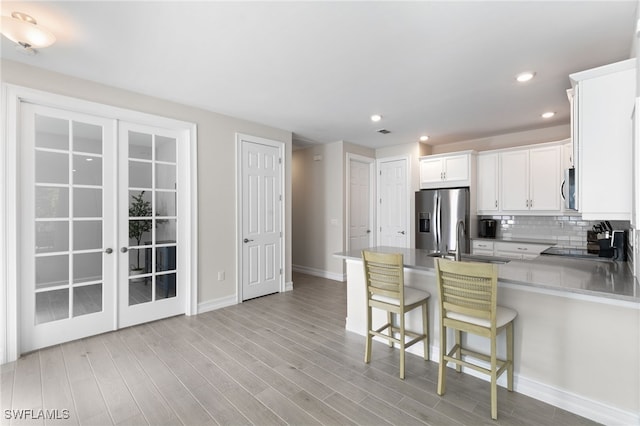 kitchen with a kitchen bar, tasteful backsplash, light wood-type flooring, stainless steel appliances, and white cabinets