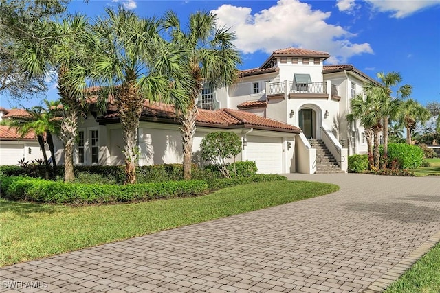 mediterranean / spanish house with stucco siding, a tile roof, decorative driveway, a front yard, and a balcony