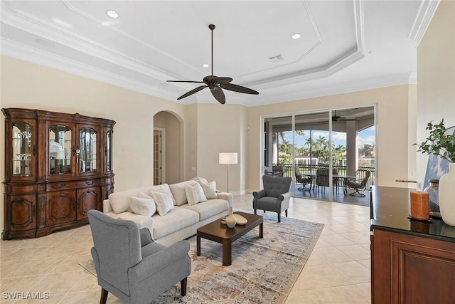 living area with ornamental molding, a tray ceiling, arched walkways, light tile patterned floors, and ceiling fan