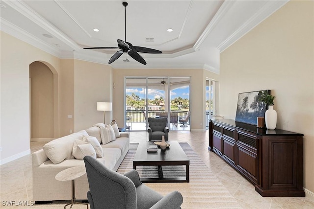 living room featuring ceiling fan, arched walkways, a raised ceiling, and ornamental molding