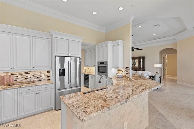 kitchen with a sink, stainless steel appliances, arched walkways, and ornamental molding