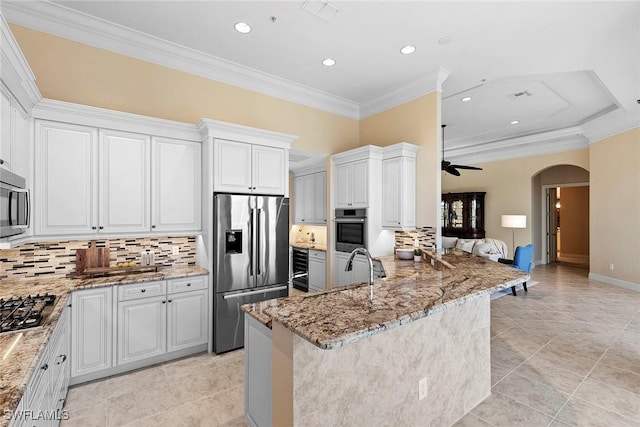 kitchen featuring arched walkways, appliances with stainless steel finishes, crown molding, light stone countertops, and ceiling fan