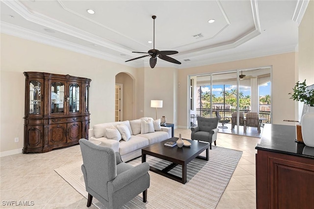 living room with a raised ceiling, crown molding, a ceiling fan, and arched walkways