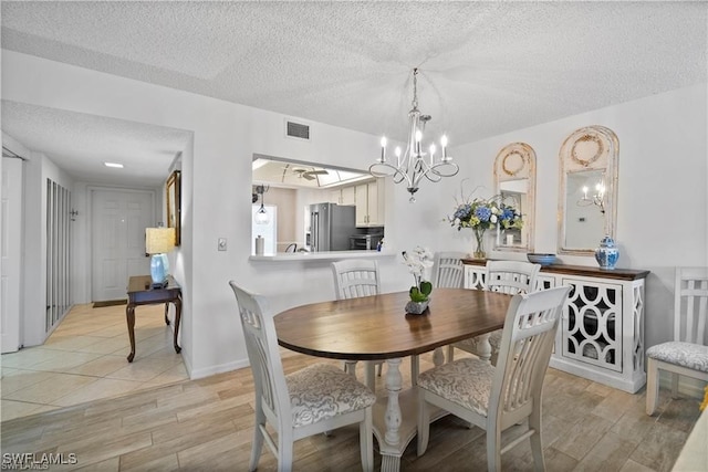 dining space featuring an inviting chandelier, a textured ceiling, and light wood-type flooring