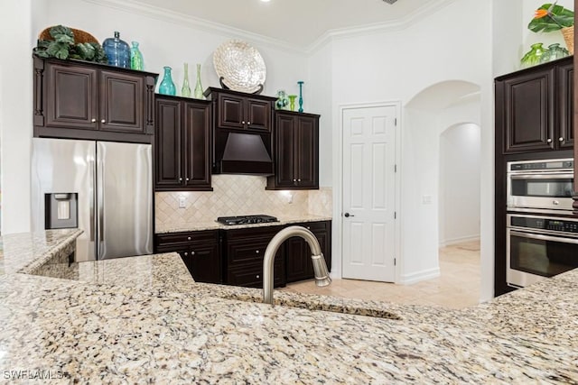 3273 Runaway Ln, Naples, FL 34114 - kitchen with stainless steel appliances, custom range hood, arched walkways, a sink, and light stone countertops