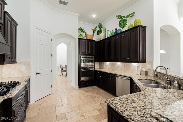 3273 Runaway Ln, Naples, FL 34114 - kitchen with stainless steel appliances, arched walkways, a sink, light stone counters, and crown molding