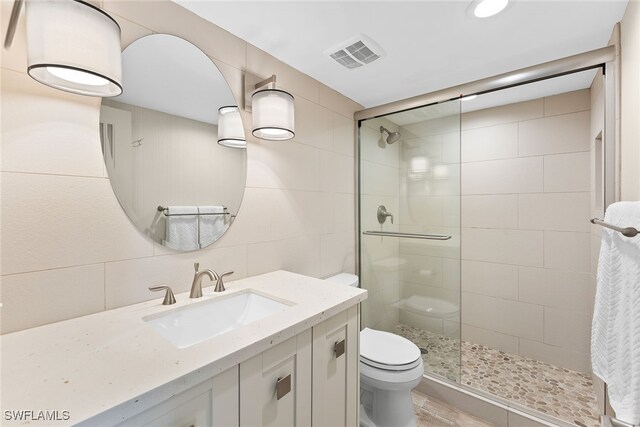 bathroom with tasteful backsplash, toilet, vanity, a shower with shower door, and tile walls