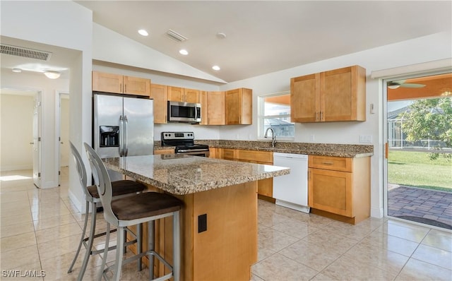 kitchen with a healthy amount of sunlight, a kitchen island, appliances with stainless steel finishes, and vaulted ceiling