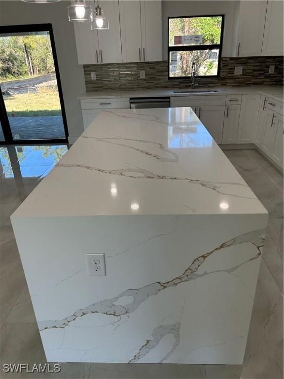 kitchen featuring sink, a kitchen island, decorative light fixtures, and light stone counters