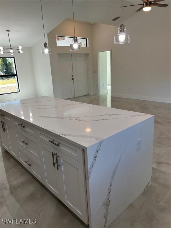 kitchen with a kitchen island, white cabinets, light stone countertops, and hanging light fixtures