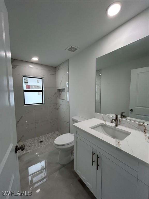 bathroom featuring vanity, tiled shower, and toilet