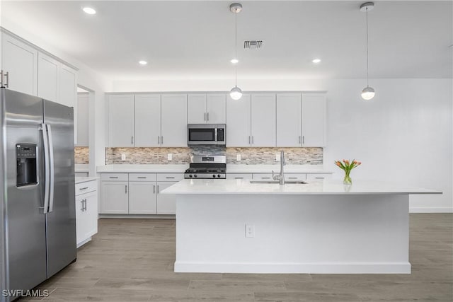 kitchen featuring appliances with stainless steel finishes, sink, white cabinets, hanging light fixtures, and an island with sink