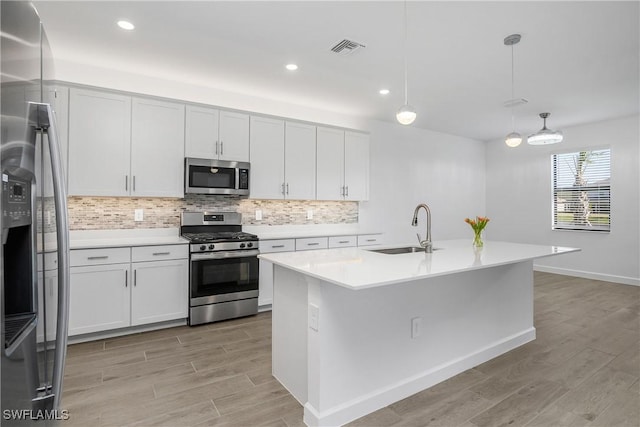 kitchen featuring appliances with stainless steel finishes, sink, a center island with sink, white cabinetry, and hanging light fixtures