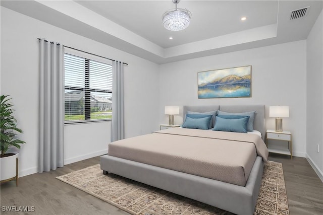 bedroom with a notable chandelier, a raised ceiling, and wood-type flooring