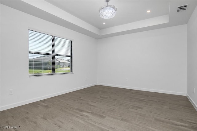 spare room with a raised ceiling, wood-type flooring, and an inviting chandelier