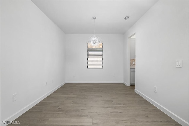 spare room featuring wood-type flooring and a chandelier