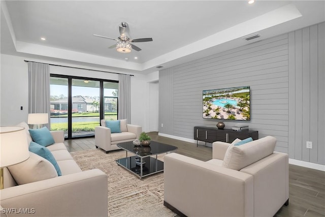 living room featuring ceiling fan, wood-type flooring, and a tray ceiling