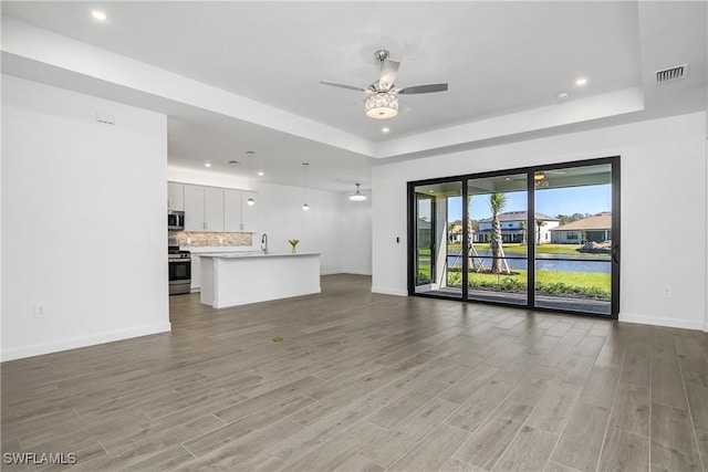 unfurnished living room with a tray ceiling, light hardwood / wood-style flooring, ceiling fan, and sink