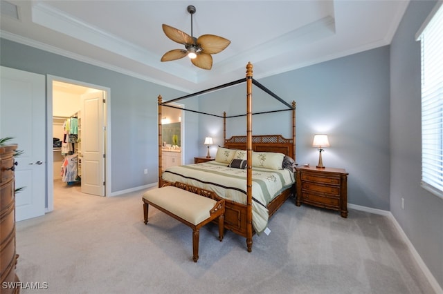 carpeted bedroom with a raised ceiling, ornamental molding, connected bathroom, and ceiling fan