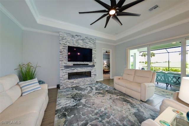 living room featuring crown molding, ceiling fan, a tray ceiling, and a stone fireplace