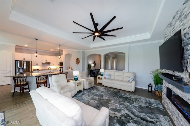 living room featuring ceiling fan, ornamental molding, a tray ceiling, and sink