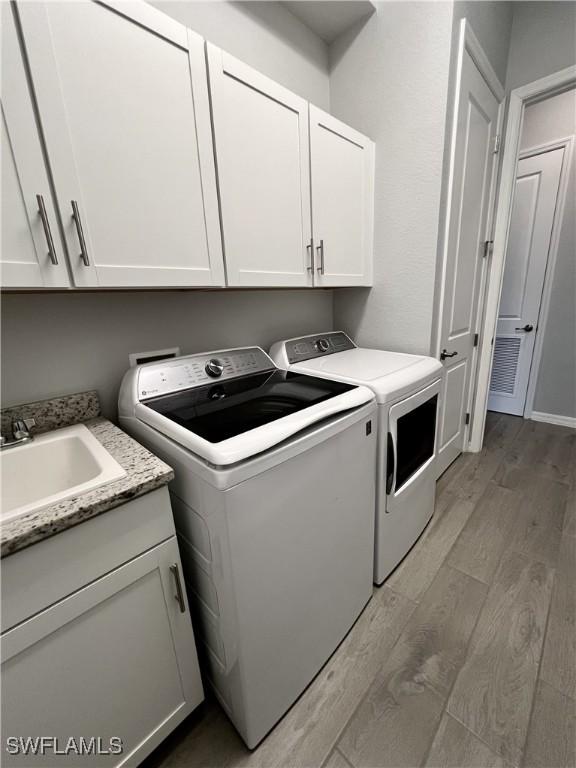 laundry area featuring cabinets, sink, washing machine and clothes dryer, and light hardwood / wood-style flooring