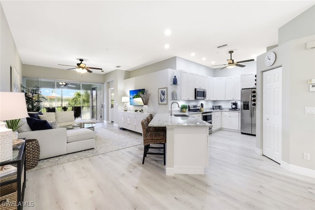 kitchen featuring stainless steel appliances, open floor plan, a sink, light stone countertops, and a peninsula