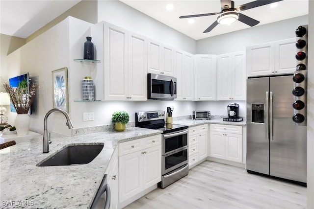 kitchen with white cabinets, sink, appliances with stainless steel finishes, light hardwood / wood-style floors, and light stone counters