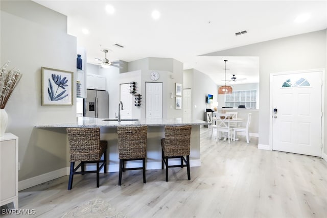 kitchen featuring kitchen peninsula, stainless steel fridge, light hardwood / wood-style floors, white cabinetry, and a breakfast bar area