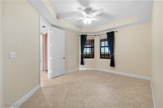 tiled spare room featuring a raised ceiling and ceiling fan