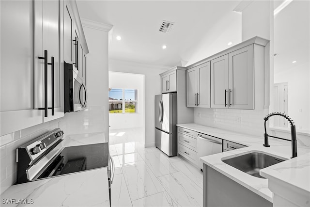 kitchen with gray cabinetry, backsplash, sink, light stone countertops, and appliances with stainless steel finishes