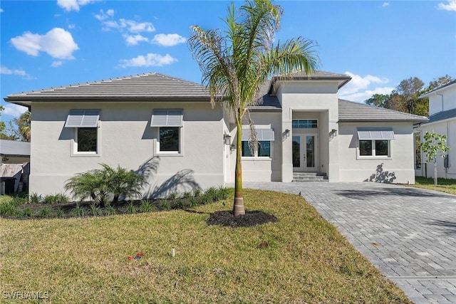 view of front facade featuring french doors, a front lawn, a tiled roof, and stucco siding