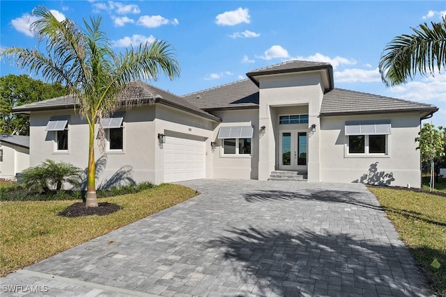 prairie-style house featuring an attached garage, french doors, decorative driveway, stucco siding, and a front yard