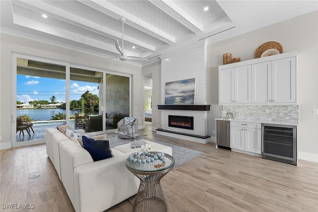 living area with beverage cooler, a large fireplace, a water view, light wood-style floors, and beam ceiling