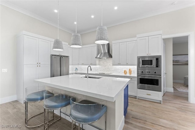 kitchen with wall chimney range hood, stainless steel appliances, light countertops, and decorative light fixtures