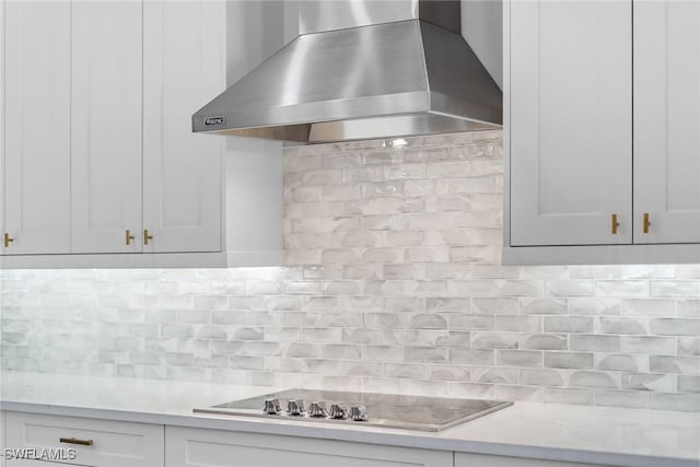 kitchen with tasteful backsplash, white cabinets, light stone counters, black stovetop, and wall chimney range hood