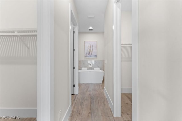 hallway featuring light wood-style floors, visible vents, and baseboards