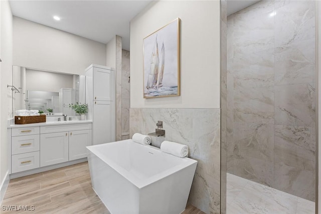 bathroom featuring a soaking tub, wood finished floors, vanity, a walk in shower, and tile walls