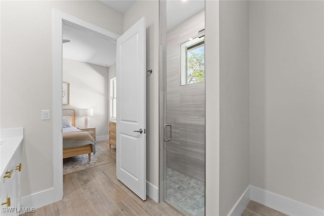 ensuite bathroom with connected bathroom, vanity, a shower stall, wood finished floors, and baseboards