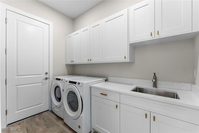 clothes washing area with separate washer and dryer, a sink, cabinet space, and light wood-style floors