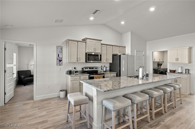 kitchen with a kitchen bar, lofted ceiling, an island with sink, and appliances with stainless steel finishes