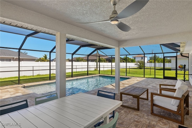 view of pool with a lawn, glass enclosure, ceiling fan, and a patio area