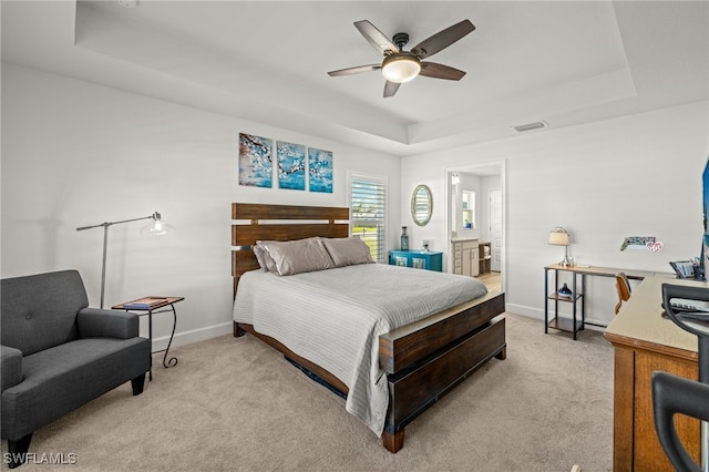 bedroom featuring ensuite bathroom, ceiling fan, light carpet, and a tray ceiling