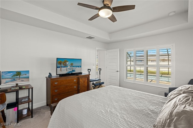 carpeted bedroom featuring a tray ceiling and ceiling fan