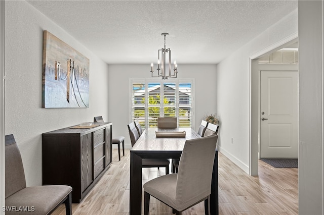 dining space with light hardwood / wood-style flooring, a textured ceiling, and an inviting chandelier