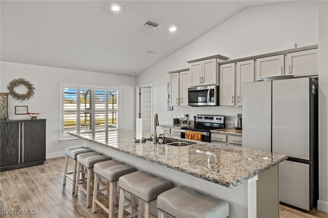 kitchen featuring sink, light hardwood / wood-style flooring, vaulted ceiling, an island with sink, and stainless steel appliances