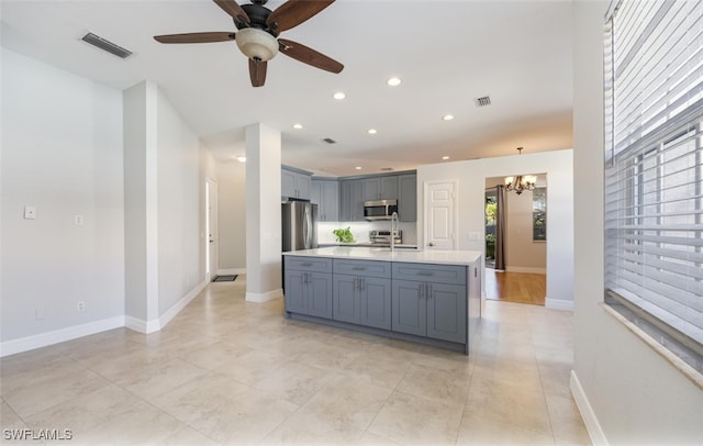 kitchen with appliances with stainless steel finishes, ceiling fan with notable chandelier, a kitchen island with sink, sink, and decorative light fixtures