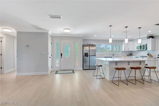 kitchen with decorative light fixtures, white cabinetry, appliances with stainless steel finishes, and light hardwood / wood-style flooring