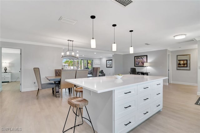 kitchen featuring light wood finished floors, a center island, white cabinetry, light countertops, and crown molding